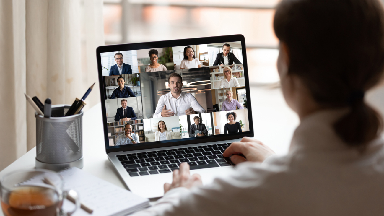 View over businesslady shoulder seated at workplace desk look at computer screen where collage of many diverse people involved at video conference negotiations activity, modern app tech usage concept